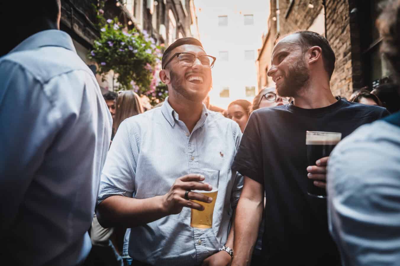 Two men laughing with pints in a sunlit alley outside St Christopher's Pub on Borough High Street, London Bridge