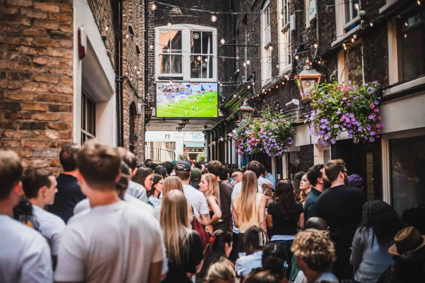 A large crowd watching live football on an outdoor screen in an alley near St Christopher's Pub, Borough High Street