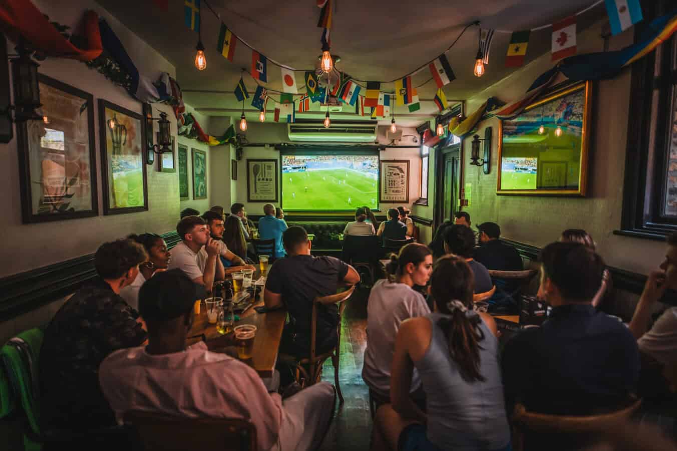 Fans seated watching live football on a large projector screen inside St Christopher's Pub, Borough High Street, London Bridge